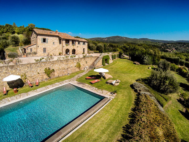 Cortona large  villa with a pool and surrounding greenery under a clear blue sky.